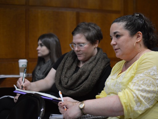 Three women sit in a conference room taking notes. They are very attentive.